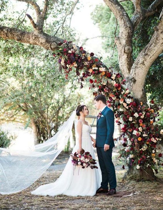 a wedding tree with a trunk fully decorated with burgundy, red, orange and other bold blooms