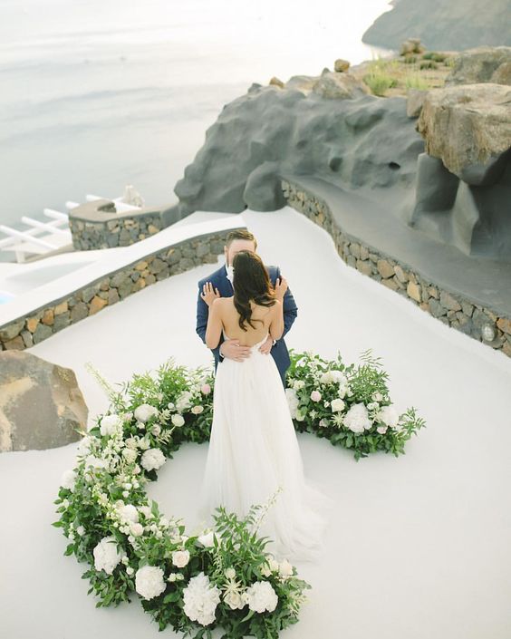 a chic and lush wedding altar with greenery and white blooms on high roof on Santorini for a wow look