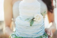 02 a ruffled ombre wedding cake from white to blue, with greenery and a neutral flower