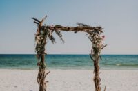 03 a boho driftwood wedding arch with blush blooms and some herbs plus candle lanterns around