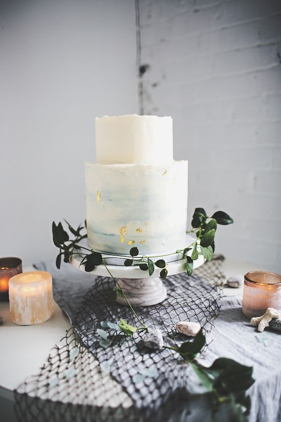 an ombre light blue wedding cake with a raw edge and gold leaf for a seaside wedding