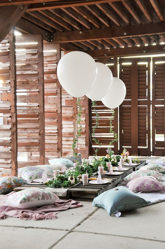 a garden bridal shower picnic inside a sunroom, greenery, white balloons and pillows right on the floor