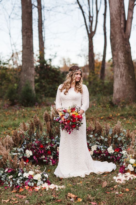a gorgeous boho fall wedding altar with dried grasses and leaves, greenery and plum-colored blooms