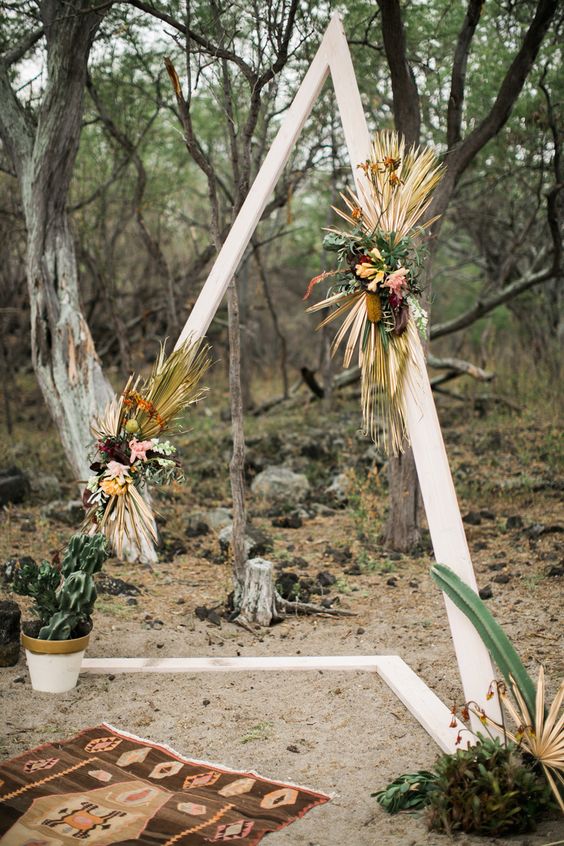 a triangle wedding arbor decorated with bold blooms, dried tropical leaves, herbs and succulents for a desert feel