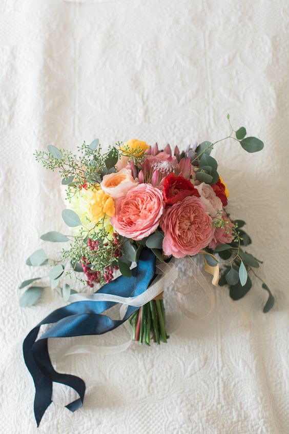 a bright bouquet in pink, yellow, red with eucalyptus and navy ribbons for a colorful summer wedding