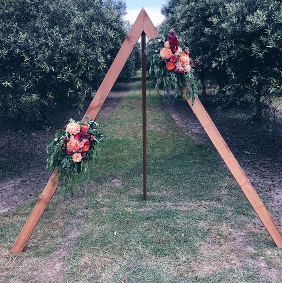 a triangle wedding arch with lush bright flowers and foliage for a garden boho wedding