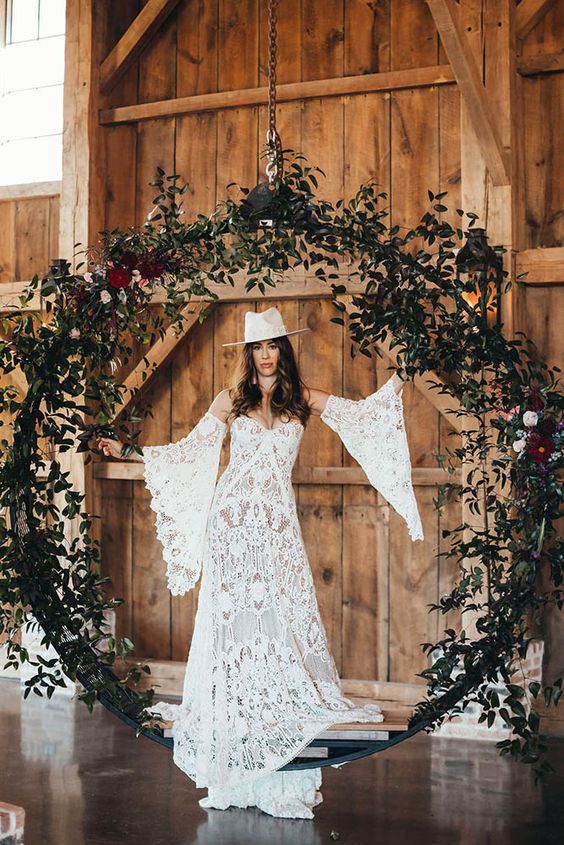 a boho bride wearing a boho lace wedding dress with bell sleeves and a white hat