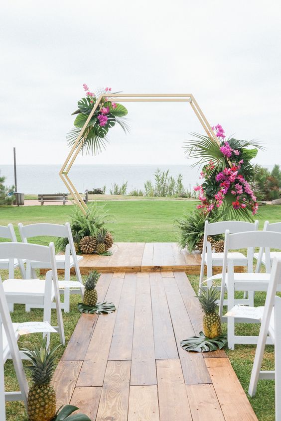 a hexagon tropical wedding arch decorated with lush greenery and fuchsia blooms