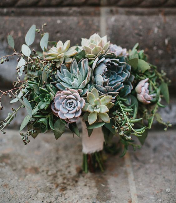 a wedding bouquet with pale grey, green and purple succulents and berries and a lace wrap