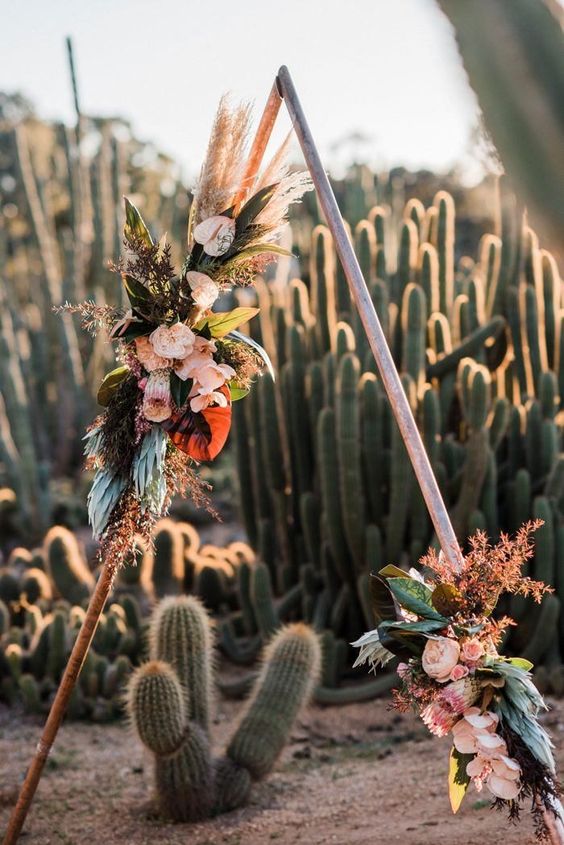 a gorgous metal triangle wedding arch decorated with leaves, pampas grass and lush large blooms for a bold look