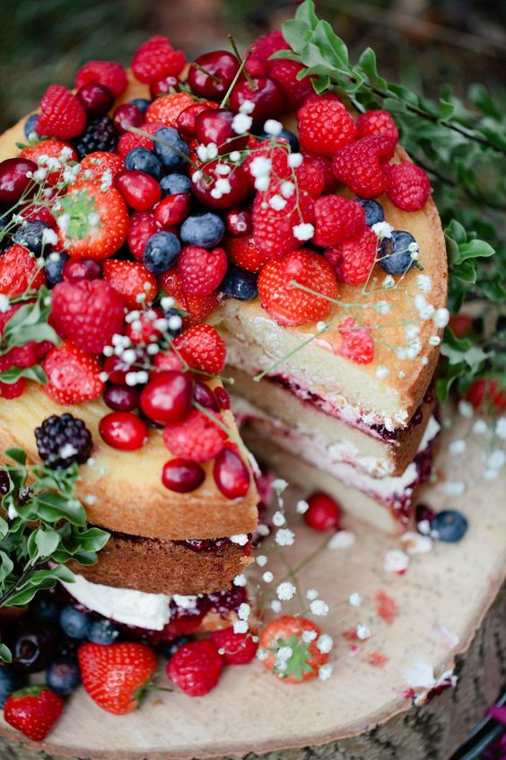 a naked wedding cake with baby's breath on top and lots of fresh berries screams summer