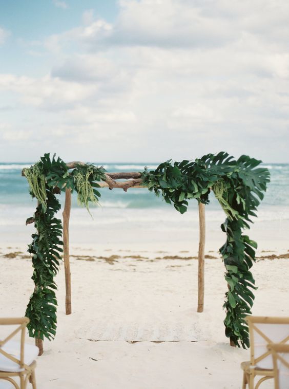 a wooden wedding arch covered fully with palm leaves for tropical beach decor
