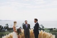 16 a gorgeous greenery, pampas grass and plum-colored bloom wedding altar for a boho feel