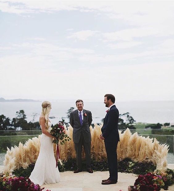 a gorgeous greenery, pampas grass and plum colored bloom wedding altar for a boho feel