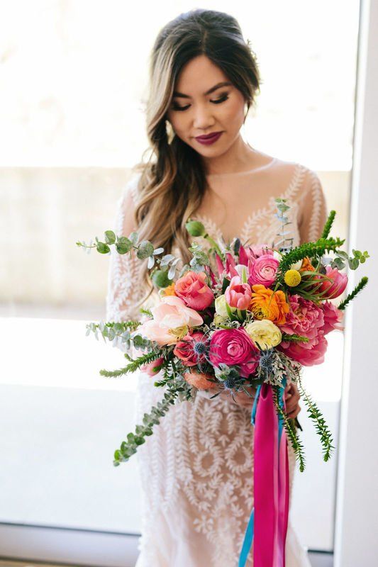 a summer wedding bouquet with pink, orange and blush flowers, greenery and colorful hanging ribbons