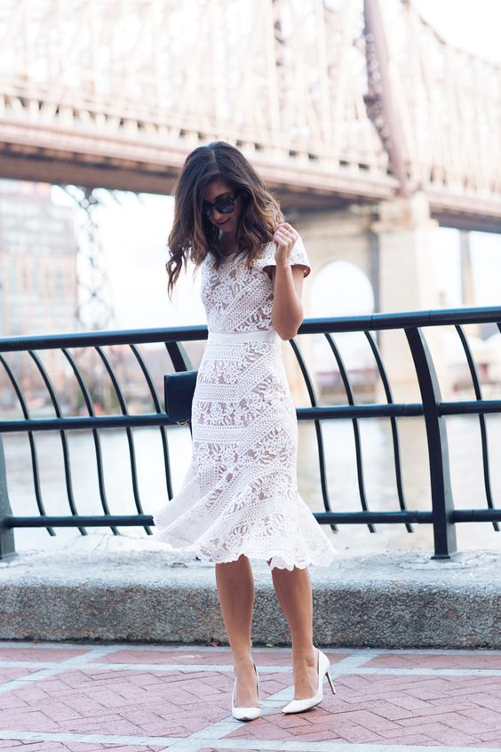 a fitting white lace midi dress with short sleeves and a ruffled skirt, white shoes and a black clutch