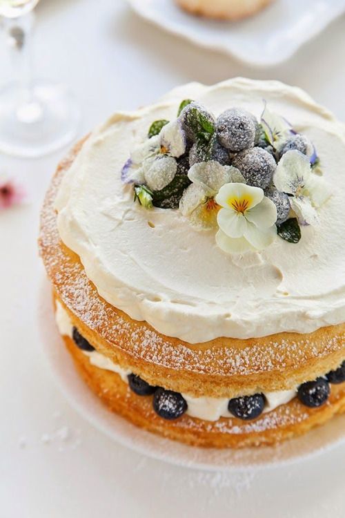 a naked wedding cake with whipped cream, sugared berries and blooms for summer
