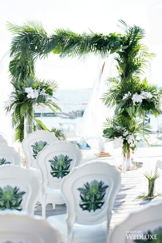 a tropical wedding arch covered with tropical leaves and with white orchids in tall vases