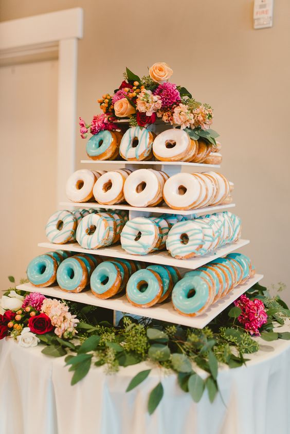 a glazed donut tower served on flowers and with flowers on top instead of a traditional wedding cake