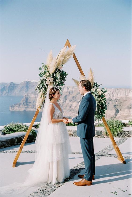 a wooden ceremony arch with creamy blooms, greenery and pampas grass for a light boho feel
