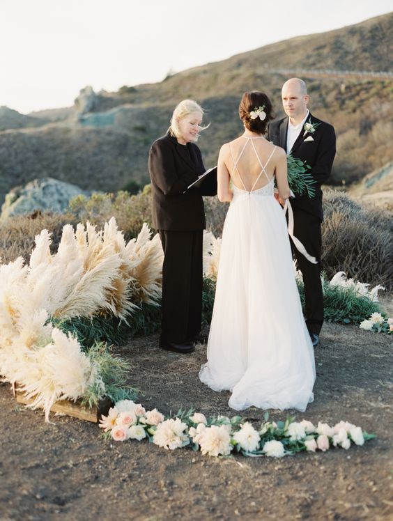 an amazing semicircular wedding altar with some blooms, greenery and pampas grass on a coast