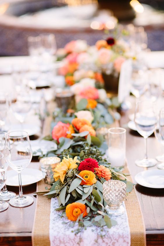 a lush eucalyptus and orange and red blooms table runner over a lace one for a bold touch