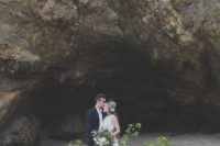 20 a lush greenery wedding arch with some white blooms and pebbles right on the beach