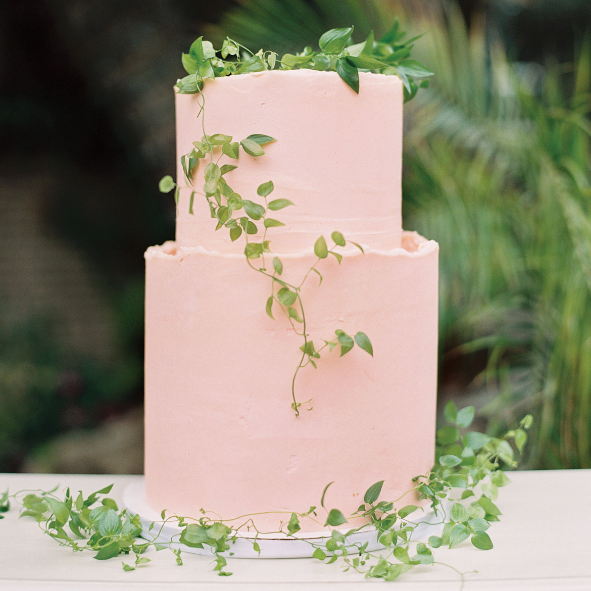 a light pink buttercream cake decorated with delicate greenery garlands on top and around is a cute idea for a dessert table