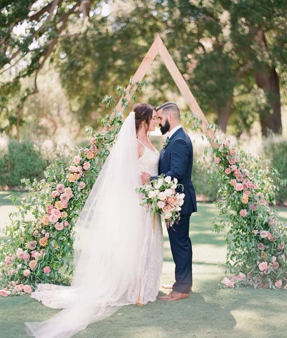 a whimsy triangle wooden arch with lush greenery and pink flowers coming up the arch