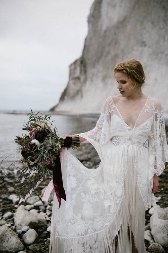 an illusion neckline wedding dress with embellishments, bell sleeves and a fringed front slit skirt