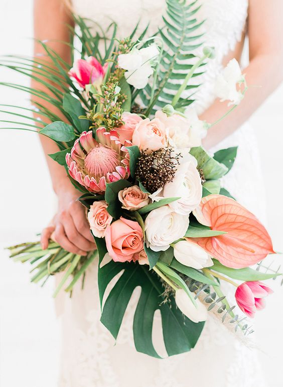 a beautiful bouquet with blush and peachy blooms, king protea and tropical leaves