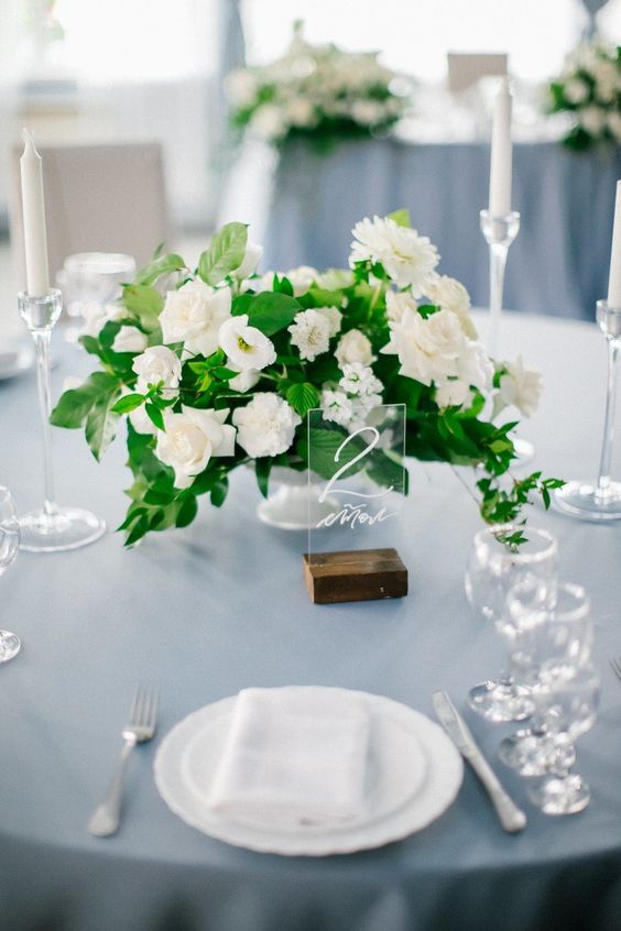 an elegant and fresh wedding centerpiece of greenery and white blooms plus an acrylic table number