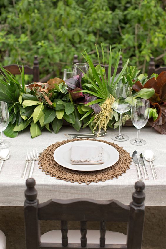a lush tropical table runner of various types of greenery and leaves for a trendy no bloom look