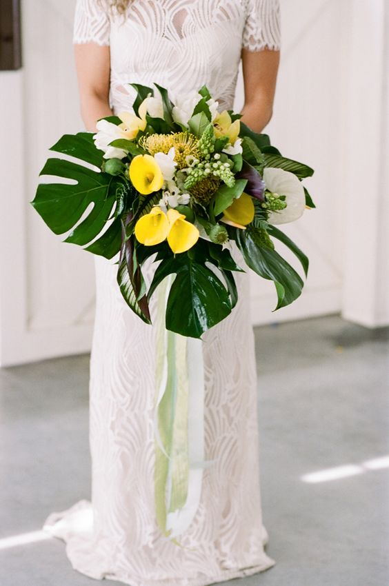 a bright bouquet with white and yellow callas and monstera leaves plus ribbons