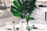 04 a minimalist tropical wedding centerpiece with clear glass bottles and tropical leaves