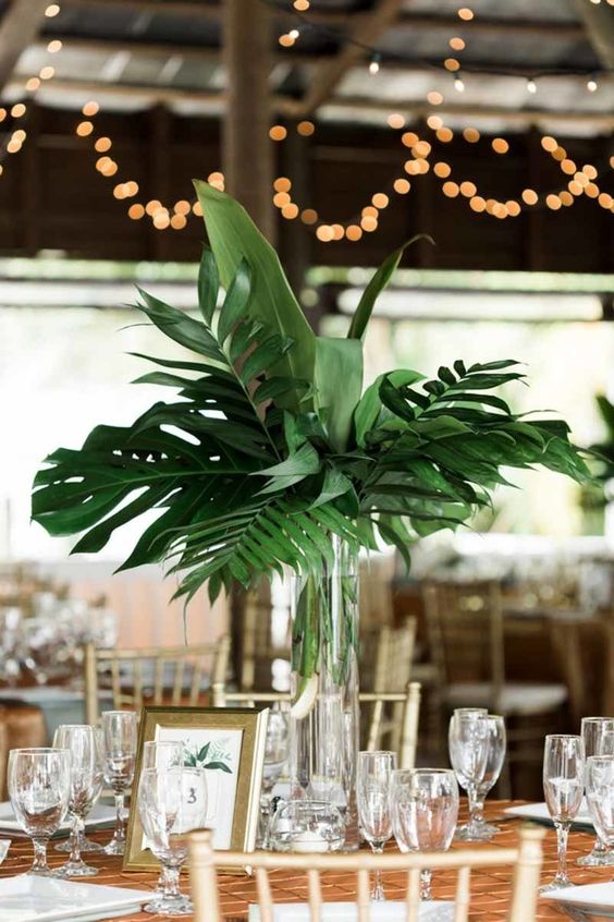 a modern tropical leaves wedding centerpiece in a clear glass vase for a cheerful feel