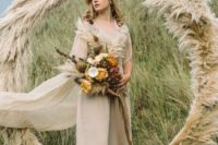 04 a taupe bridal jumpsuit with a cape and a taupe pampas grass circle wedding arch