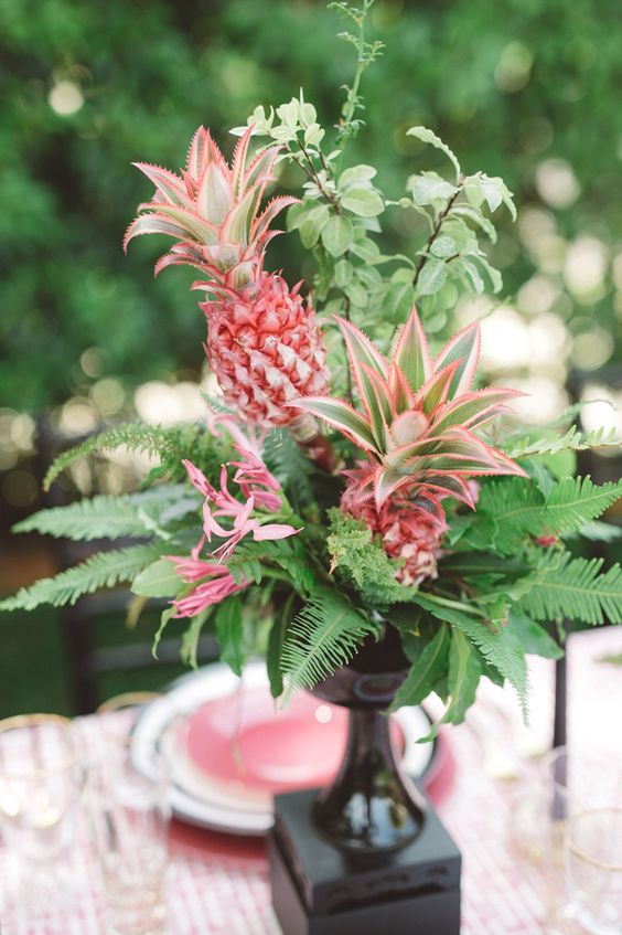 a lush tropical centerpiece of ferns, greenery and pink pineapples looks super cool