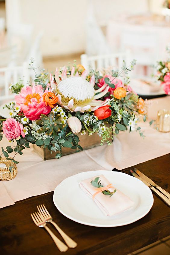 a box centerpiece with pink and red blooms, greenery, succulents and a king protea