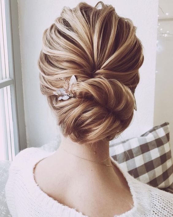 a chic and voluminous bridal chignon hairstyle with a wavy bump on top and a little floral hairpiece