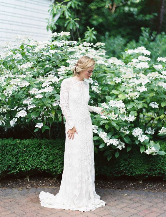 a lace sheath wedding dress with long sleeves, a high neckline, a small train and buttons for a modest look