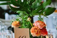 11 a centerpiece with tropical leaves, orange blooms and vintage metal jugs