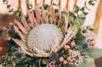 11 a creative and bold bouquet with a king protea, blue thistles, berries and little white blooms around
