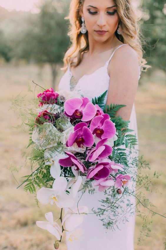 a colorful and vibrant wedding bouquet with hot pink and white orchids and textural greenery