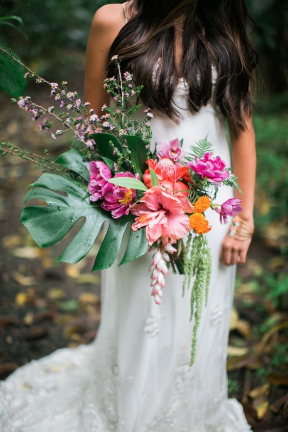 a stylish bouquet with a monstera leaf, pink, fuchsia and orange blooms and some cascading greenery
