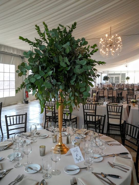 a tall greenery wedding centerpiece shaped as a ball on a tall gilded stand