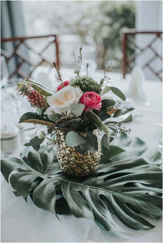 a cool centerpiece of a gilded pineapple, white and pink blooms, greenery and a little pineapple