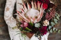16 a fall boho wedding bouquet with a vertical shape, a king protea, burgundy and plum blooms, herbs and greenery plus a bow