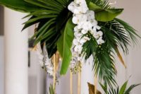 16 a glam tropical centerpiece of large tropical leaves and white orchids on tall gilded stands