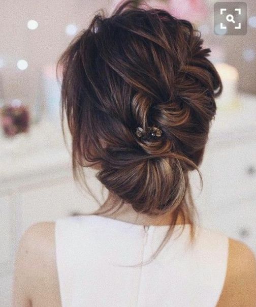 a diagonal braided low bun with bangs and a rhinestone hairpiece for a chic modern touch